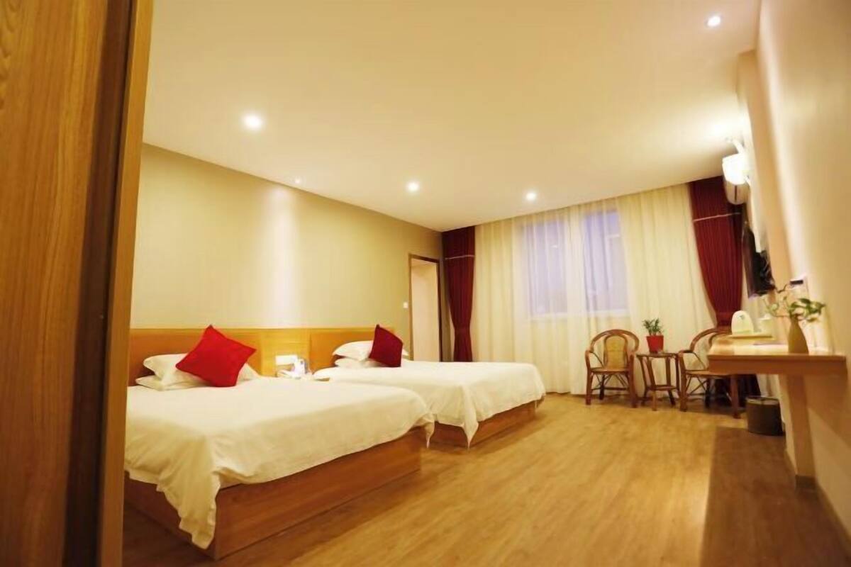 A hotel room with two beds, a desk, chairs, and a window with curtains.