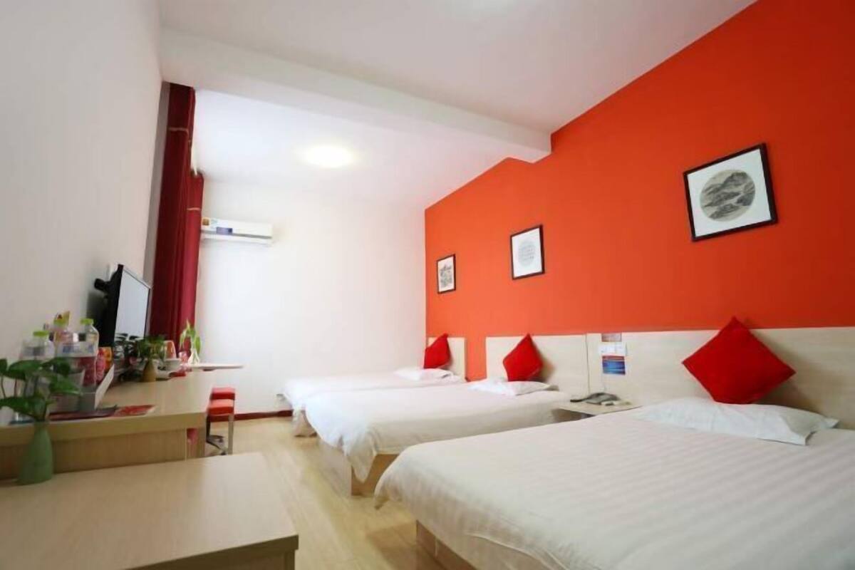A hotel room with two beds, a desk, a red curtain, and a wall-mounted air conditioner.