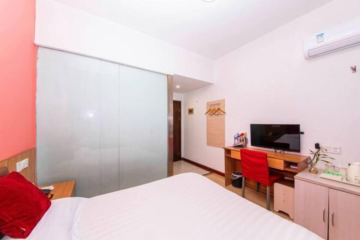 A hotel room with a bed, a desk with a TV, a wardrobe, and a sliding door.