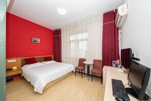Een hotelkamer met een bed, twee stoelen, een bureau met een computer en een airconditioning.