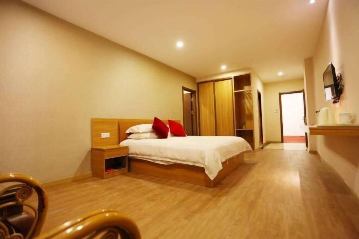 A bedroom with a bed, wooden wardrobe, and a TV on the wall.