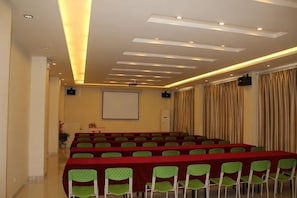 A conference room with a long table, green chairs, a projector screen, and a whiteboard.