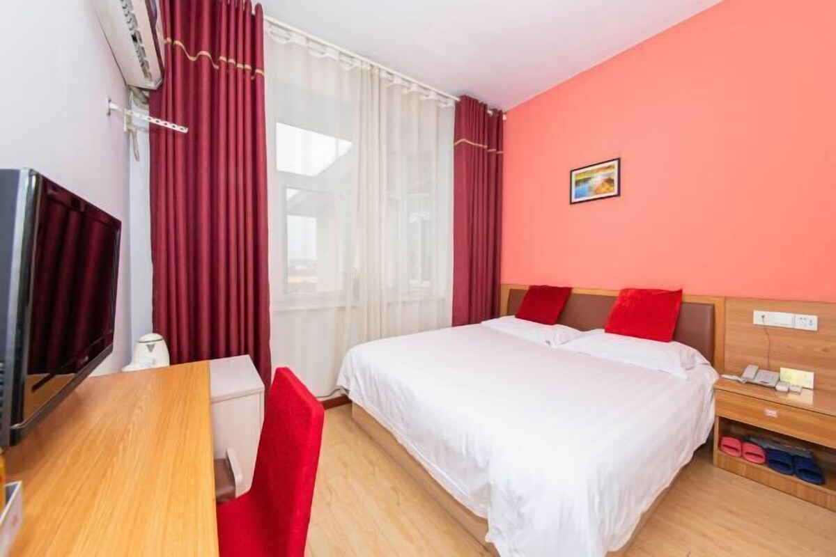 Een hotelkamer met een bed, een bureau, een stoel, een televisie en een klein plankje met slippers.