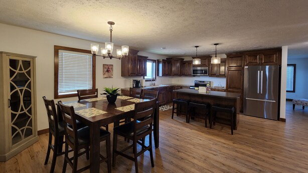 A spacious kitchen with wooden cabinets, a large island, and a dining area with chairs and a table. - Perfect for a TEAM of people! (Hastings)