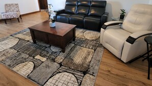 A living room with a black leather sofa, a white armchair, a dark wooden coffee table, and a patterned rug. - Perfect for a TEAM of people! (Hastings)