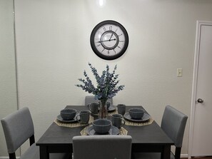 A dining table with a clock above it, surrounded by chairs and set with bowls and cups.