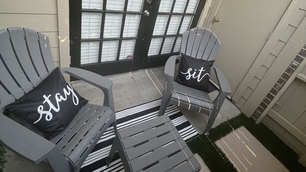 Un patio con dos sillas Adirondack, una mesita y una puerta negra con paneles de vidrio esmerilado.