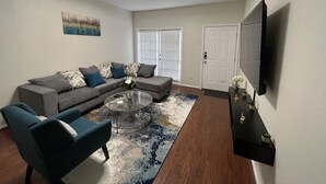 Una sala de estar con un sofá modular, dos sillones, una mesa de centro, un televisor y una puerta con ventanal.