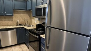 Una cocina moderna con electrodomésticos de acero inoxidable, armarios azul oscuro y suelo de baldosas.