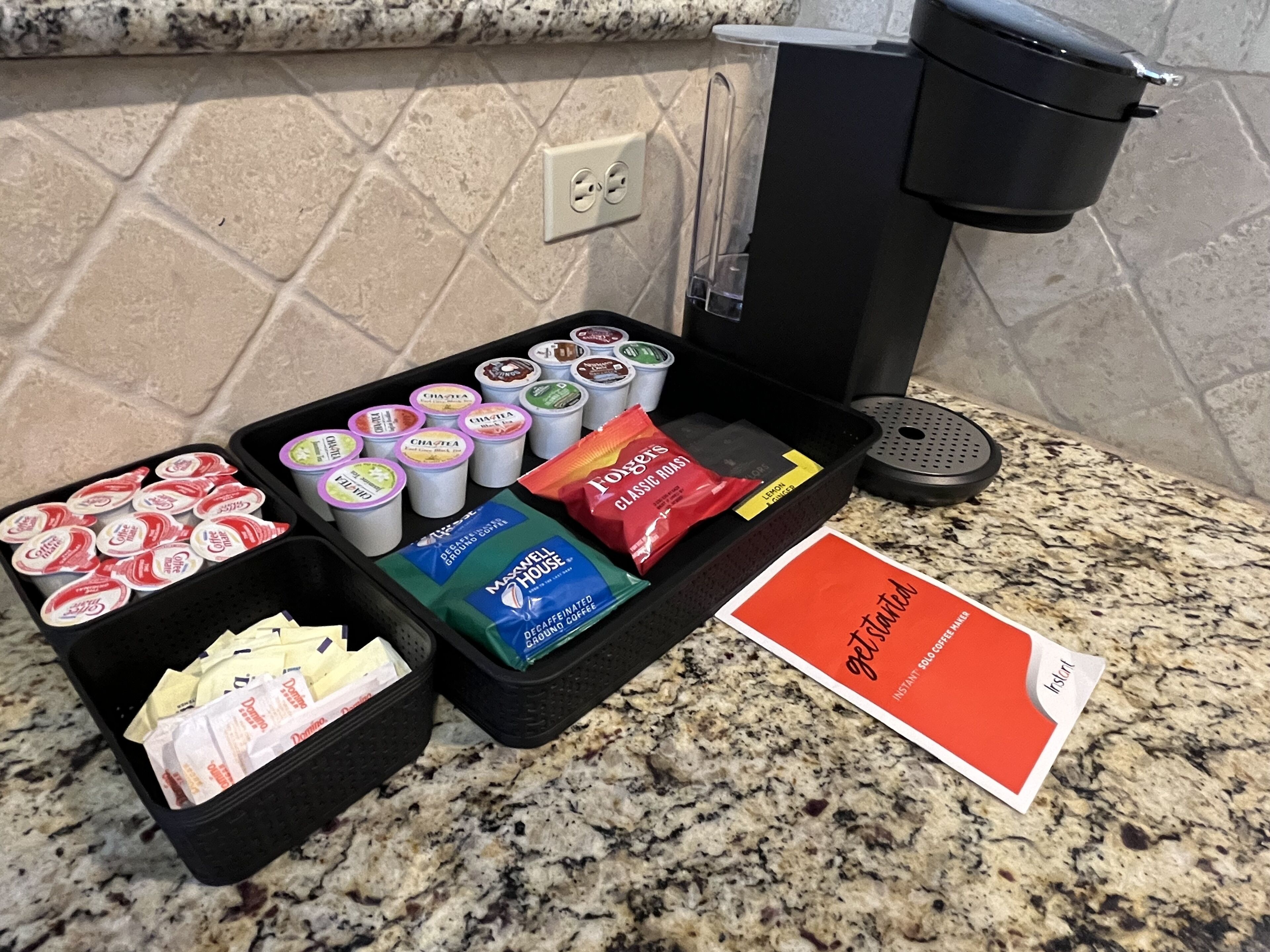 A coffee station with various coffee pods, a packet of instant coffee, and a sign.