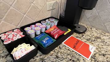 A coffee station with various coffee pods, a packet of instant coffee, and a sign.