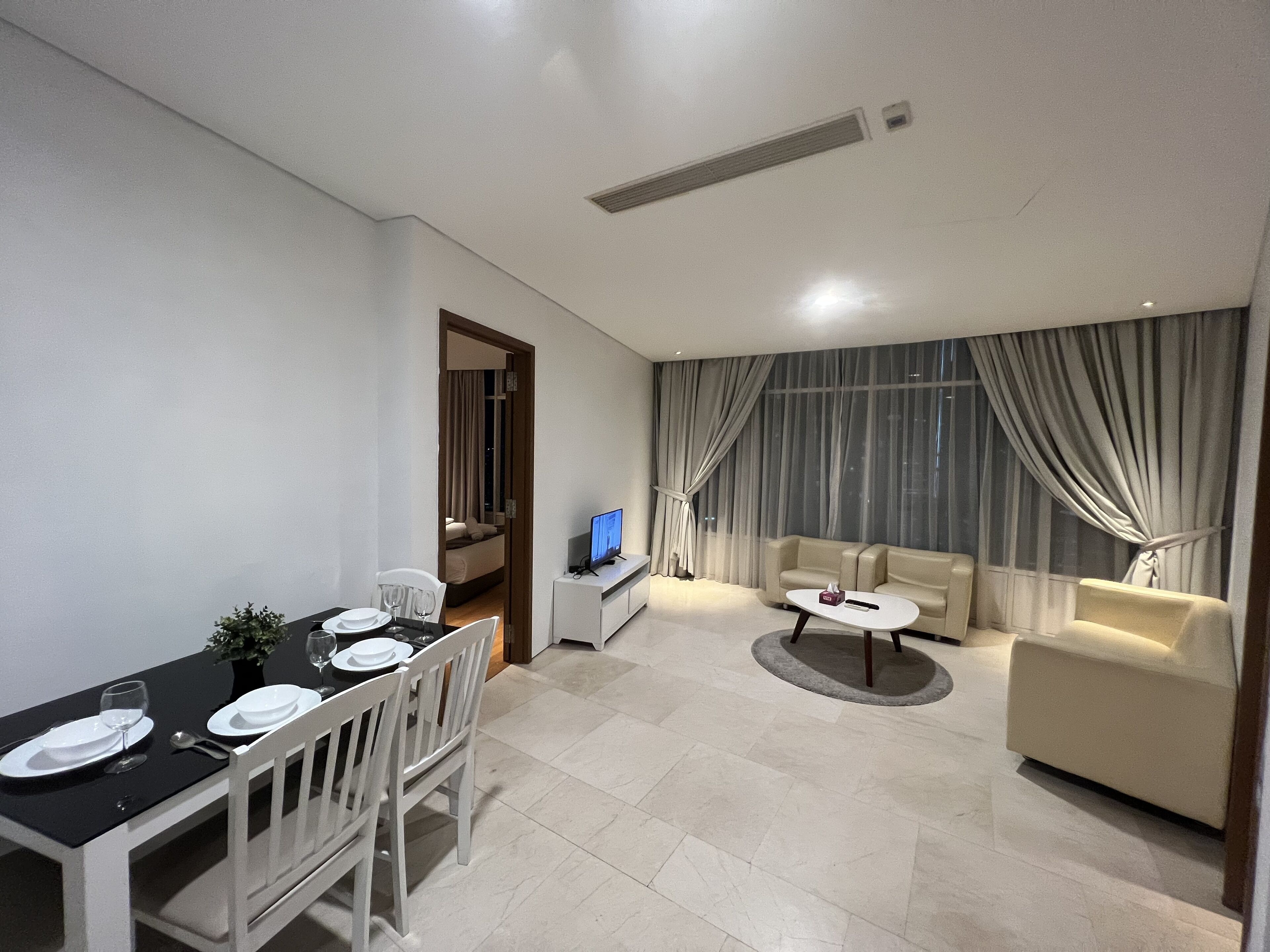 Uma sala de estar moderna com área de jantar, um sofá, uma TV e uma janela com cortinas.