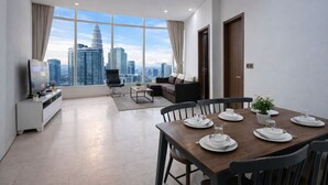 A modern living room with a city view, a dining area with a table set for four, and a seating area with a sofa and a chair. - Vortex Suites KLCC by Luna (Kuala Lumpur)