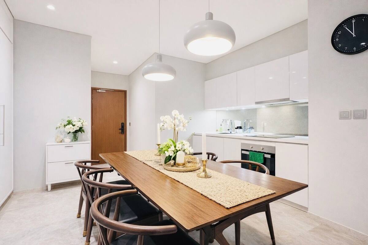 Une cuisine moderne avec des meubles blancs, une table à manger en bois et des luminaires suspendus.