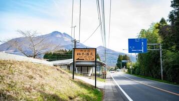 Una señal de tráfico con texto en japonés, una montaña al fondo y un edificio con un cartel.