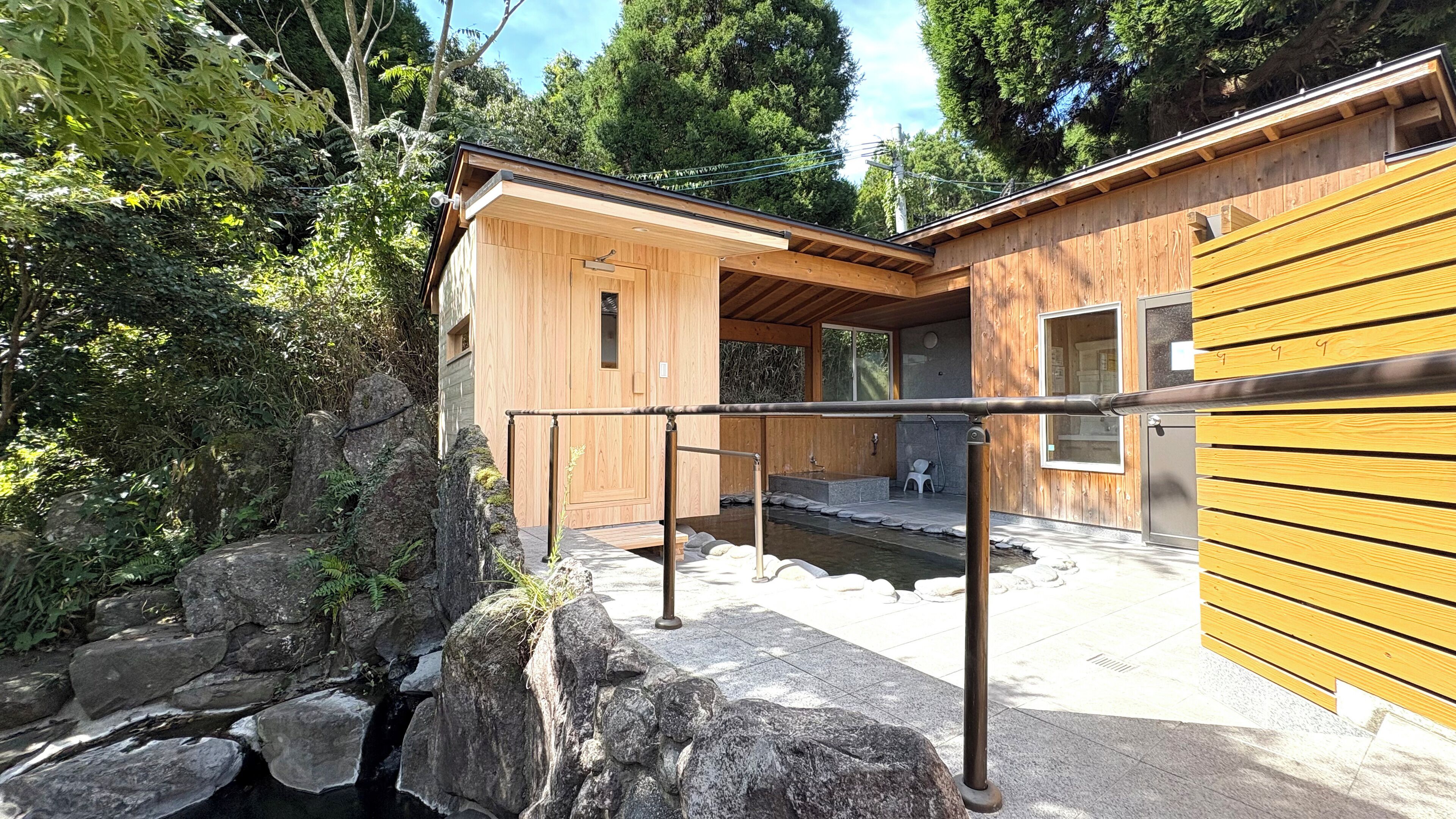 A wooden cabin with a stone pathway leading to a small pond, surrounded by dense greenery.