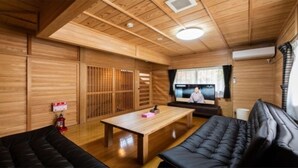 A traditional Japanese-style room with wooden walls and floors, a tatami mat floor, a low table, black leather sofas, and a television. - YUFUIN O-YADO YUKI ONSEN (Yufu)
