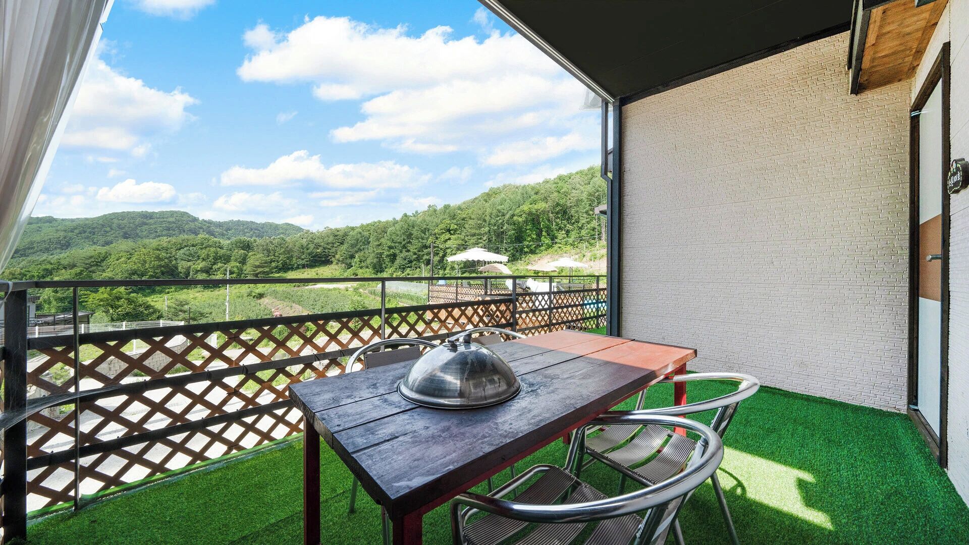 A balcony with a table and chairs, a view of green hills, and a wooden fence.