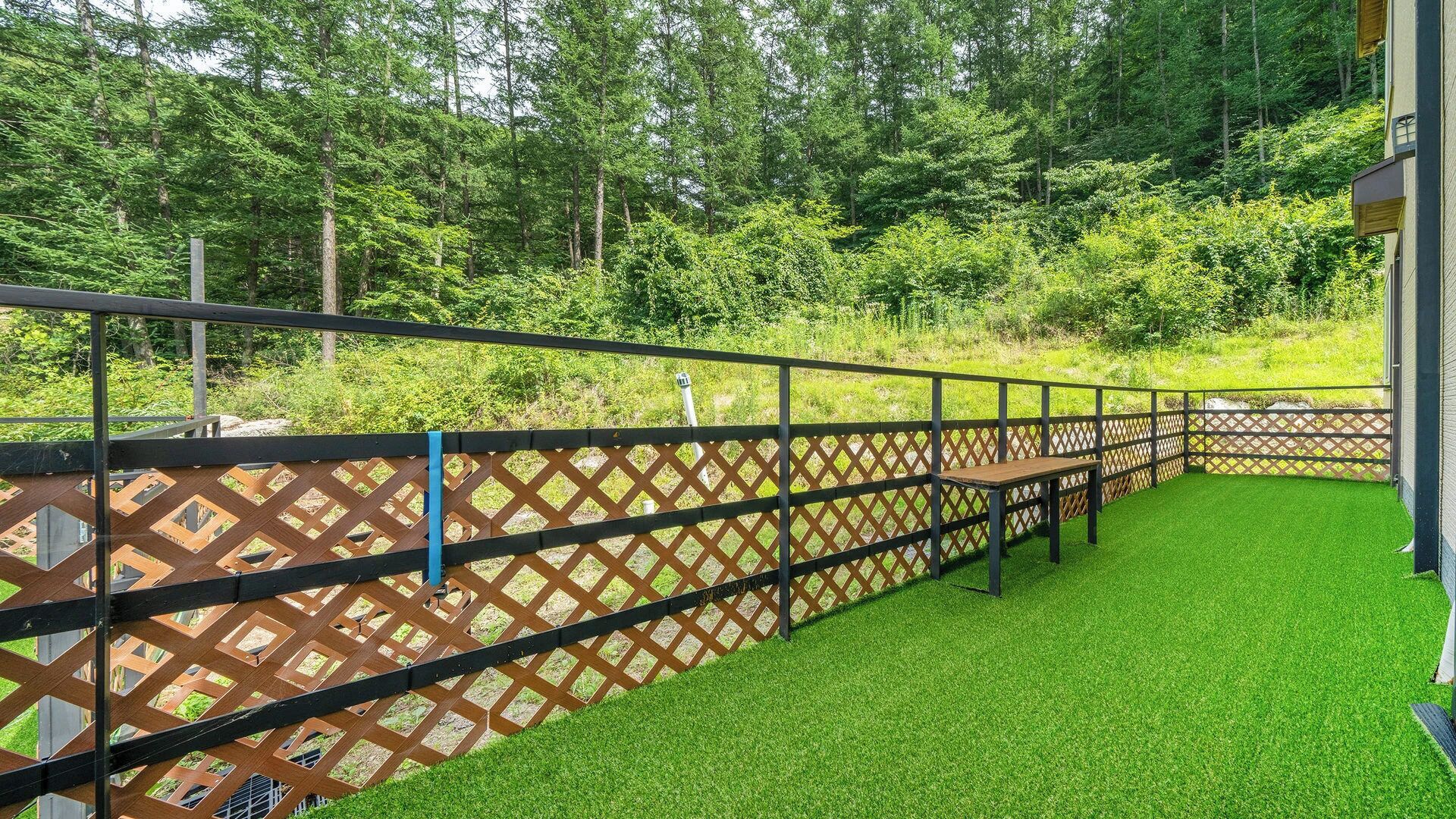 An outdoor area with a wooden fence, artificial grass, and a bench.