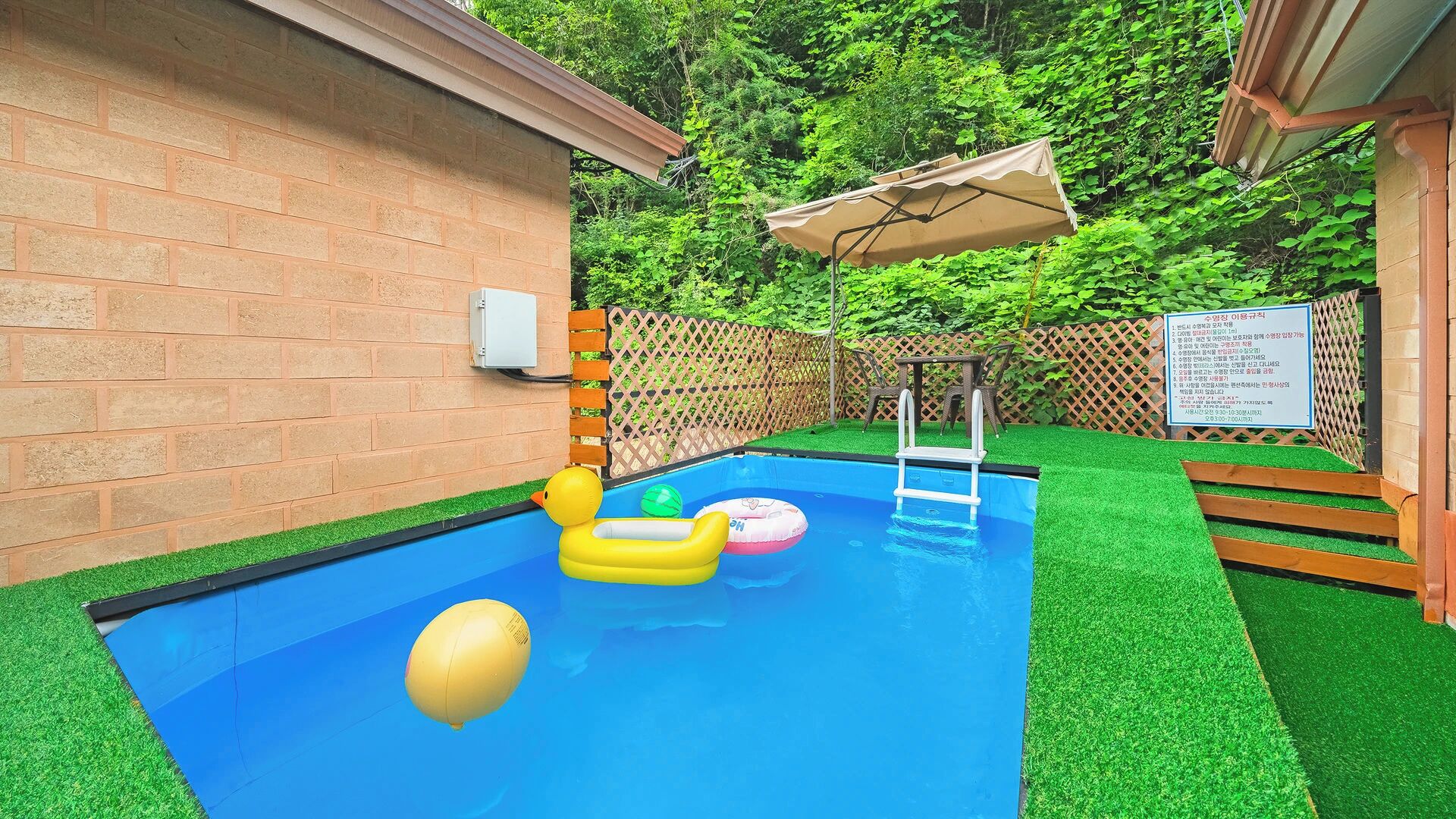 Une piscine avec des jeux gonflables, une échelle et une terrasse en bois, avec une clôture et de la verdure en arrière-plan.