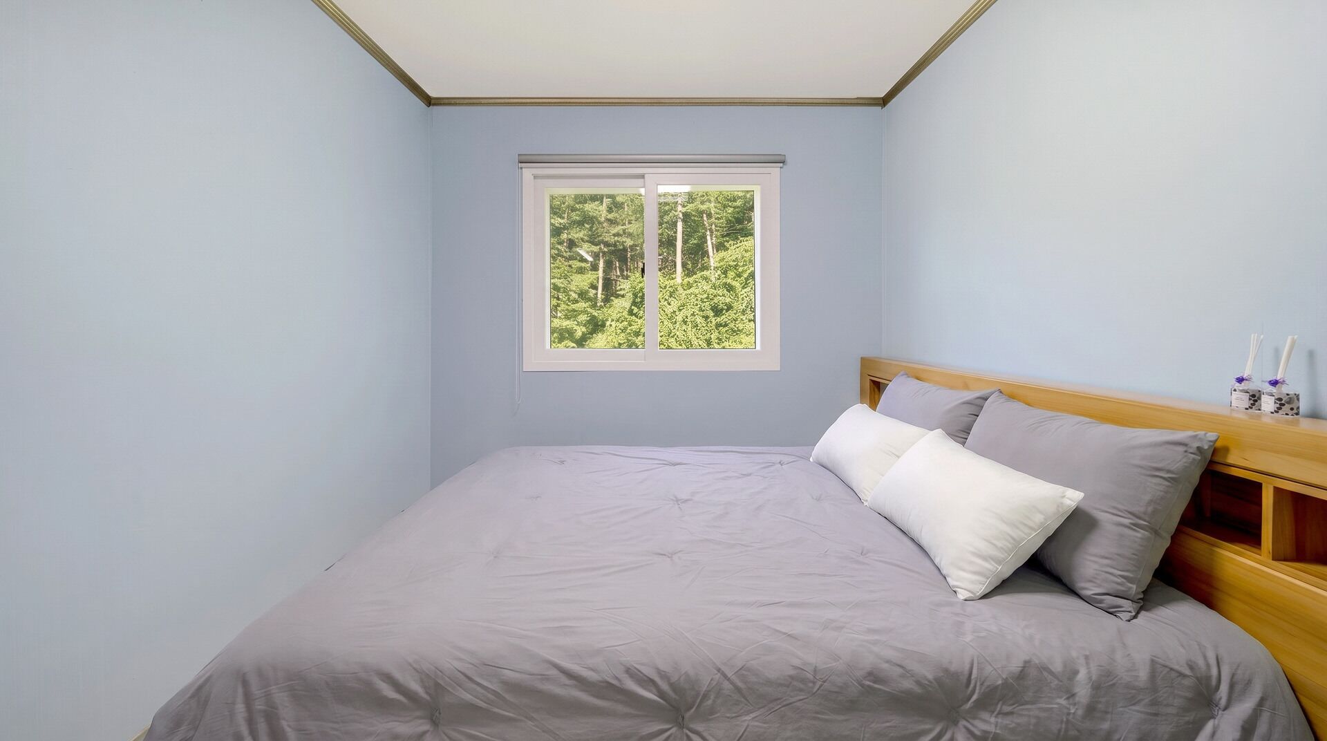 Une chambre à coucher avec un lit, une fenêtre donnant sur des arbres et une table de chevet avec des bougies.