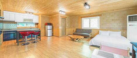 A compact room with a kitchenette, a bed, a sofa, and a small table.