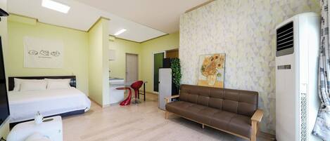 A hotel room with a bed, a sofa, a small dining area, and a kitchenette.