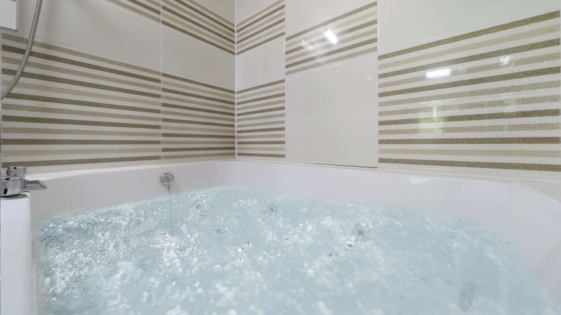 A bathtub with running water, surrounded by striped wall tiles.