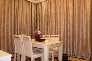 A dining area with a table and chairs, a vase with flowers, and a curtain backdrop.