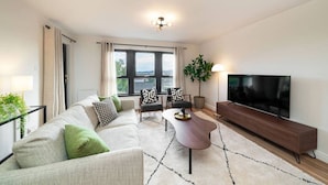 Un salon moderne comprenant un canapé, des fauteuils, une table basse, un téléviseur et une grande fenêtre donnant sur un paysage agréable.