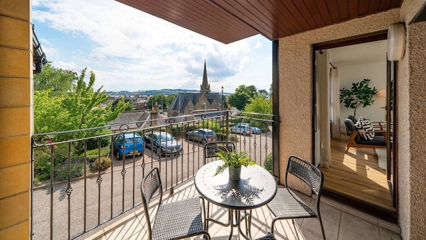 Un balcon avec une table et des chaises, une vue sur une église et des voitures garées.