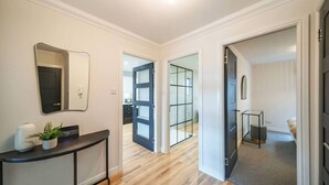 Un couloir avec une console, un miroir et une plante en pot. Deux portes donnent accès à d’autres pièces.