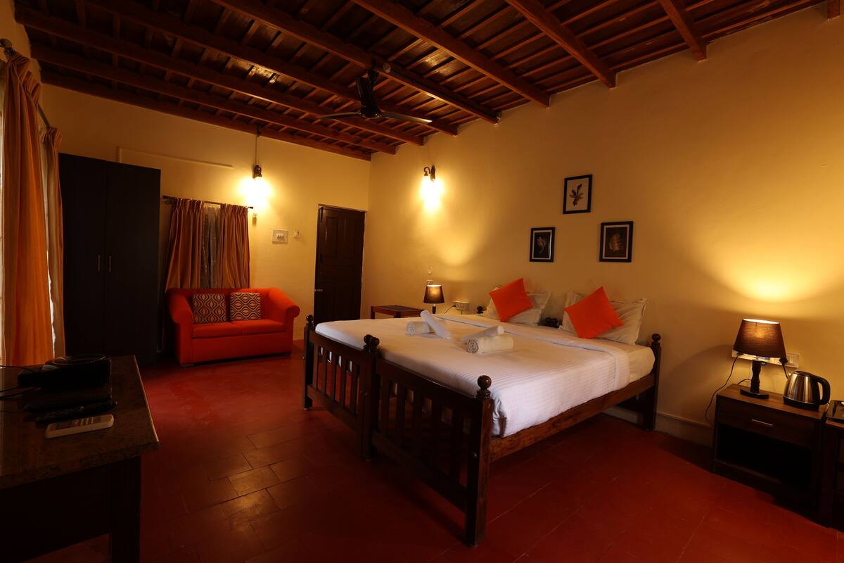 Un dormitorio con cama de madera, un sofá rojo, una mesita de noche con lámpara y techo de madera.