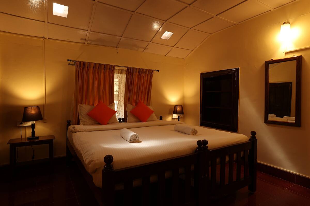 Una habitación de hotel con una cama, dos mesitas de noche, un espejo montado en la pared y un candelabro en el techo, además de una ventana con cortinas.