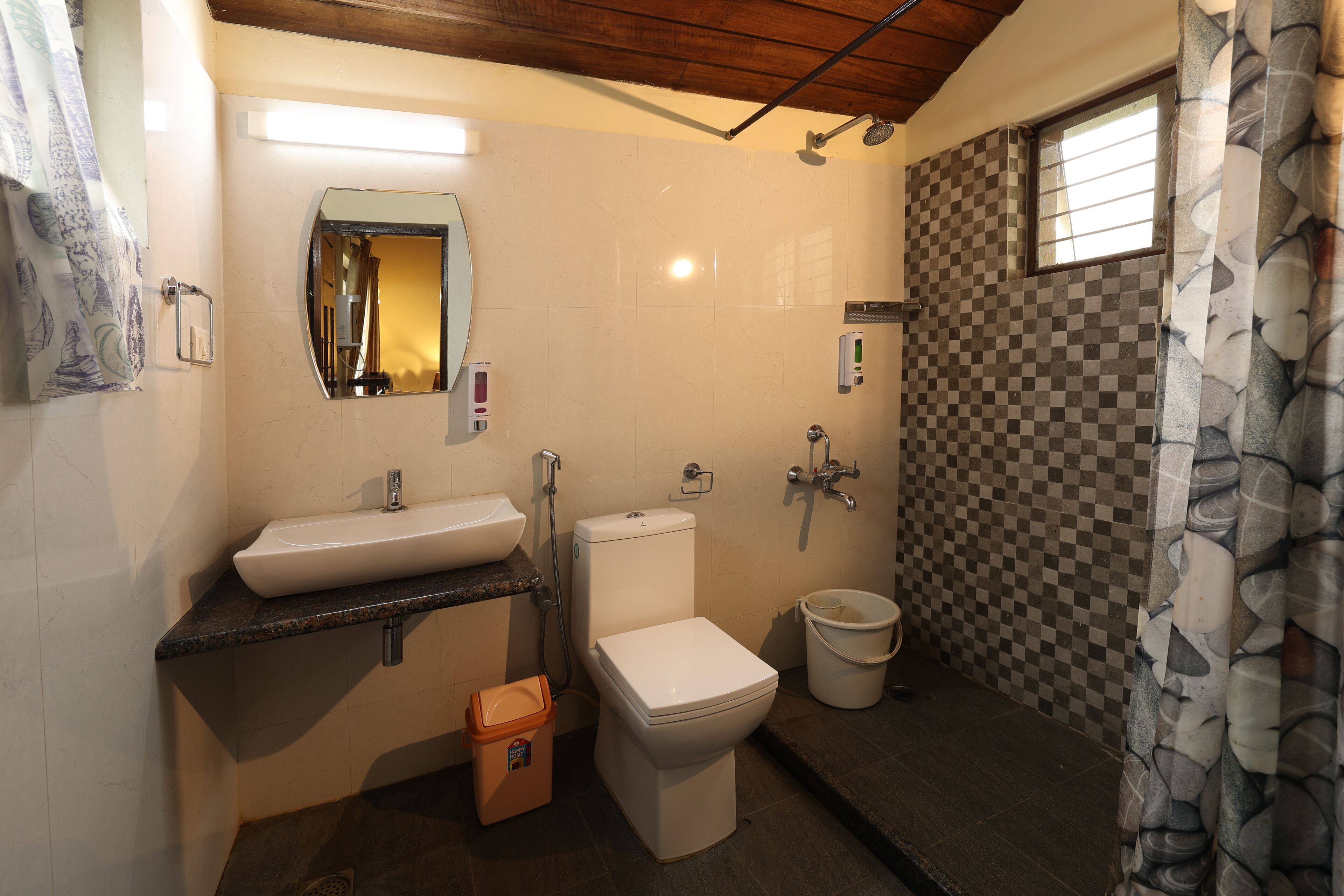 A bathroom with a sink, toilet, shower, and a bucket.