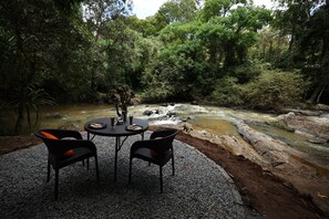 Une table avec deux chaises, donnant sur une rivière bordée de rochers et d’arbres.