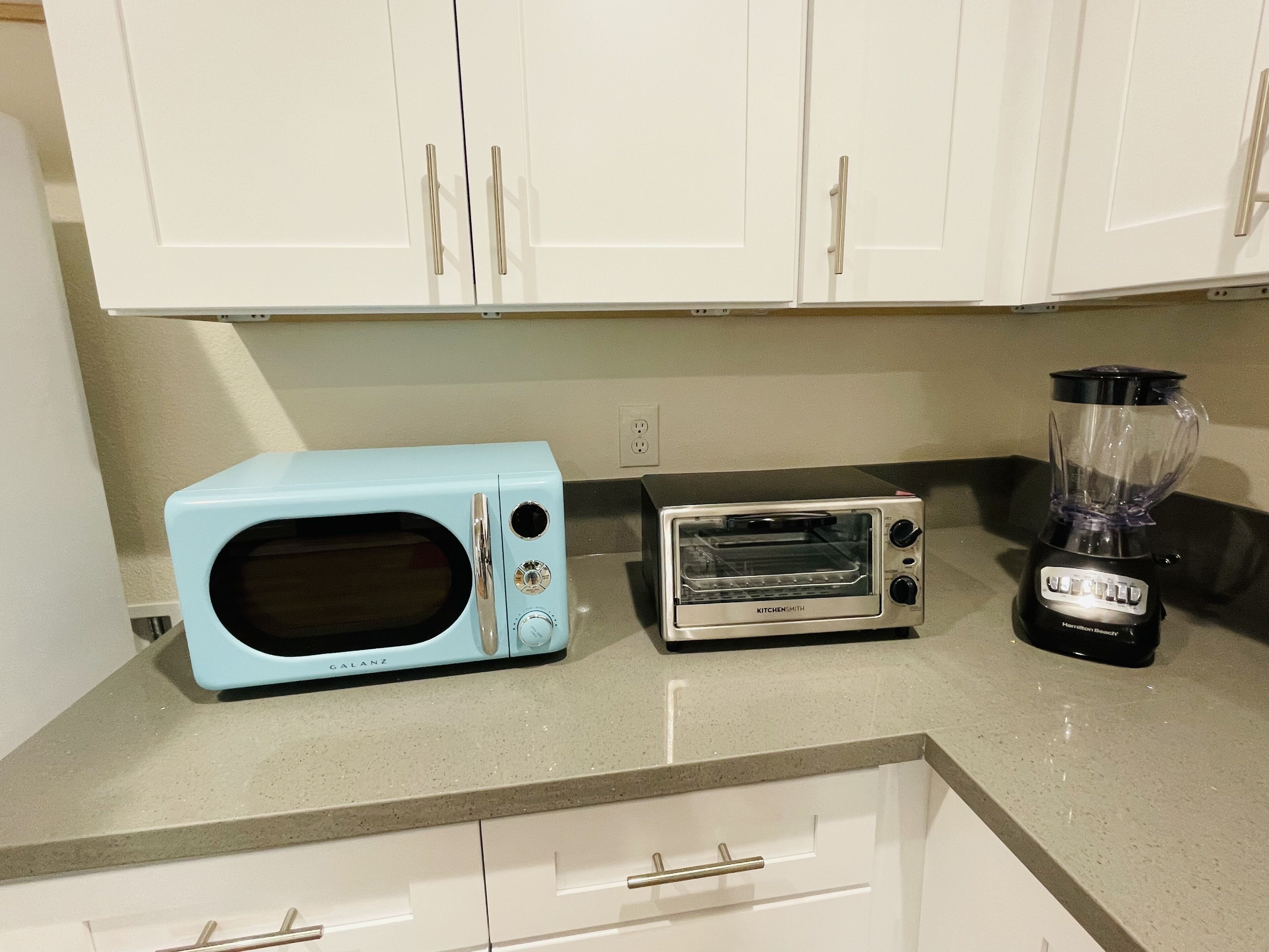 A kitchen with white cabinets, a blue microwave, a silver toaster oven, and a black blender on the countertop.