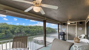 A balcony with a view of a river, wicker furniture, and ceiling fans.