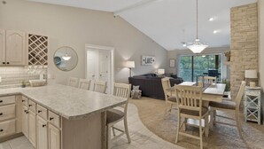 A spacious kitchen with a large island, a dining area with chairs, a sofa, and a stone accent wall.