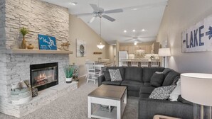 A living room with a stone fireplace, a ceiling fan, and a dining area in the background.