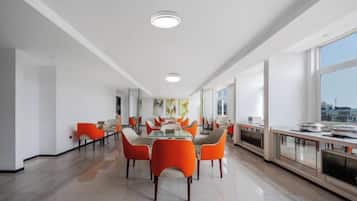 A modern dining area with a long table, orange chairs, and a city view.