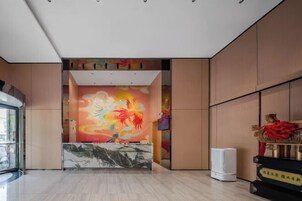 Zona de recepción de un hotel con un mural colorido, un mostrador de mármol y una pieza decorativa tradicional china.