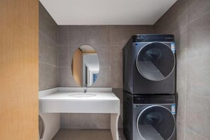 A compact bathroom with a sink, mirror, and stacked washing machines. - dinghaophotel (Taizhou)