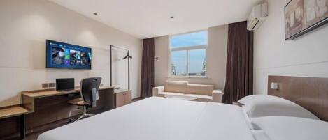 A modern hotel room with a large bed, a desk with a computer, a TV mounted on the wall, and a window with curtains.