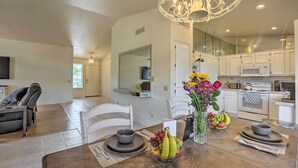 A modern kitchen with white cabinets, a microwave, and an oven. There is a dining area with a wooden table, chairs, and a vase with flowers. - Saddlebrooke Home w/ Private Pool & Amenities (Tucson)