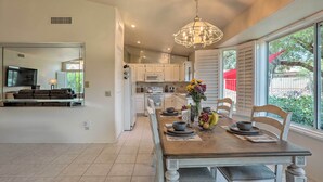 A modern kitchen with white cabinets, a dining table set for four, and a large window with a view of greenery. - Saddlebrooke Home w/ Private Pool & Amenities (Tucson)