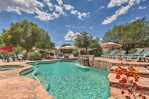 A swimming pool with a waterfall feature, surrounded by lounge chairs and umbrellas, under a clear sky.
