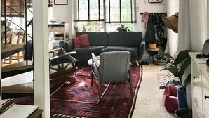 A spacious living room with a large window, a dark sofa, a patterned rug, and a staircase leading to another level. - 3 Br by park hayarkon 1min  2 Ichilov (Tel Aviv)