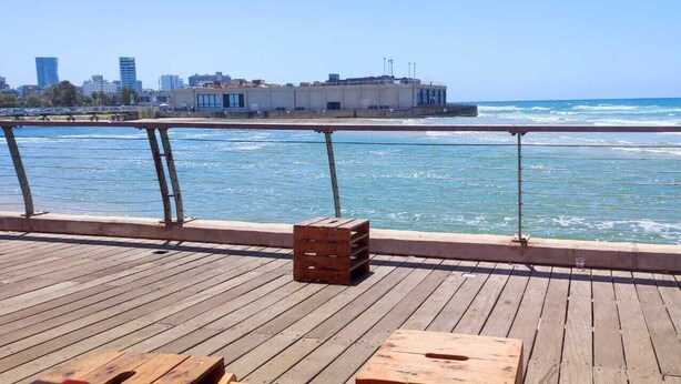 A wooden deck with a railing overlooking a body of water, a city skyline in the background, and a wooden crate on the deck. - 3 Br by park hayarkon 1min  2 Ichilov (Tel Aviv)
