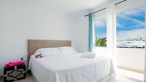 Habitación de hotel con una cama grande, una mesita de noche con una toalla rosa y vistas a la ciudad a través de un ventanal amplio.